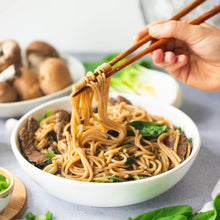 Load image into Gallery viewer, Hand holding chopsticks pulling noodles from white bowl containing beef udon stir fry
